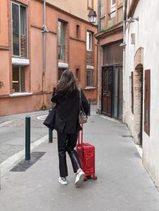 a woman walking down a street with a red suitcase at OVYO Hôtel in Toulouse