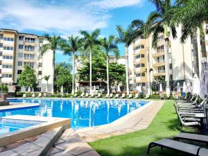 a swimming pool with chairs and palm trees and buildings at Family condo, pool, beach and surf in Jacó