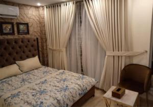 a bedroom with a bed and a chair and curtains at Bahria Prime Apartments in Lahore