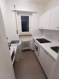 una pequeña cocina con armarios blancos y una ventana en LentulusSkyAppartement, en Berna