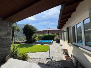 un patio con sombrilla y piscina en Casa Medusa - con piscina, a 2 minuti dalla stazione en Verscio