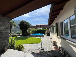 um pátio com um guarda-sol e uma piscina em Casa Medusa - con piscina, a 2 minuti dalla stazione em Verscio