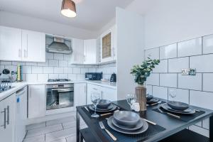 a white kitchen with a table with plates and wine glasses at Stylish House in Stalybridge with WiFi & Parking Sleeps 8 by PureStay in Stalybridge