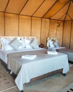 2 camas en una tienda de campaña con sábanas blancas en Sahara Safari Camp en Merzouga