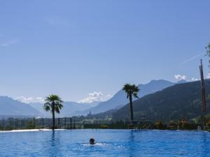 a person swimming in a pool with palm trees and mountains at Appartement Ariane in Frastanz