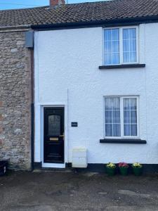 a white house with a door and two plants at Cosy cottage in Chard