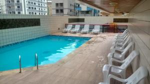 einen Pool mit Stühlen neben einem Gebäude in der Unterkunft Apto 3 quartos, churrasqueira, vista para o mar e piscina in Praia Grande