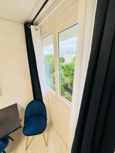 um quarto com uma cadeira azul e uma janela em T1 - Le Papangue 5* - neuf, vue jardin, 8’ airport em Sainte-Clotilde