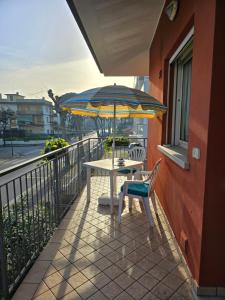 a table and a chair with an umbrella on a balcony at Appartamento Caracola in Lignano Sabbiadoro