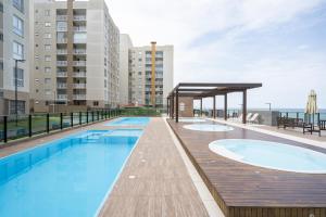 einen Pool mit einer Holzterrasse und einem Gebäude in der Unterkunft Aptos completos com vista mar pé na areia em Barra Velha em condomínio Resort com Spa, Piscina, quadra de futebol, Sala de jogos, brinquedoteca, Complexo com diversos comércios in Barra Velha + 26 Fotos