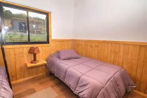Cama en habitación de madera con ventana en Wincarayen Lodge & Cabañas, en Panguipulli
