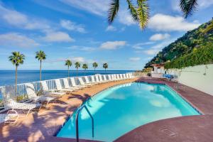 a swimming pool with chairs and the ocean in the background at Bright Catalina Island Condo with Ocean Views! in Avalon