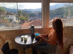 a woman sitting at a table in front of a window at La Musica Hostel OuroPreto in Ouro Preto