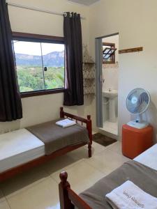 a bedroom with two beds and a window with a fan at Pousada Guiné in Mucugê