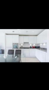 una cucina con armadi bianchi e tavolo in vetro di Amazing Apartment a Harlow