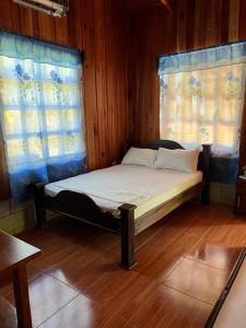Cama en habitación de madera con 2 ventanas en Cabañas Hospedaje la Reserva, en Hojancha