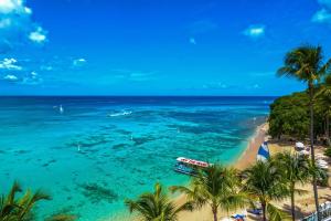 uma praia com palmeiras e um barco na água em Waves Hotel and Spa by Elegant Hotels - All-Inclusive em Saint James