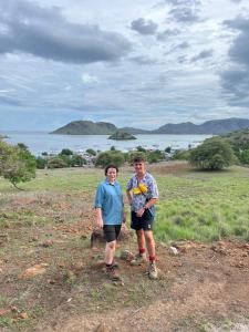 two men standing in a field with the ocean in the background at Jhuna Komodo Homestay in Komodo
