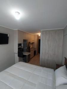 a bedroom with a large white bed and a kitchen at Departamento Centro Plaza 403 in Pitrufquén