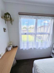 a bedroom with a window with white curtains and a desk at House of Somer in Matamata