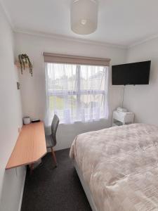 a bedroom with a bed and a desk and a window at House of Somer in Matamata