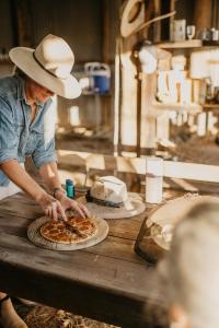 Ein Mann mit einem Cowboyhut, der eine Pizza auf dem Tisch schneidet. in der Unterkunft Gilgooma 