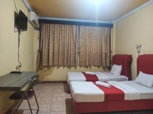 a room with two beds and a desk and a television at RedDoorz Syariah At Hotel Matahari 1 Jambi in Jambi