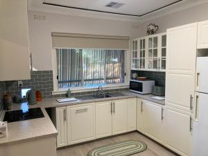 cocina con armarios blancos, fregadero y ventana en Herbert Cottage, en Tumut