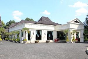 a large white building with palm trees in a courtyard at Urbanview Syariah Wisma Nabil Solo in Lawean