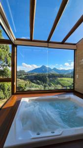 uma banheira de hidromassagem num quarto com uma grande janela em Chalés Monte das Oliveiras em Domingos Martins