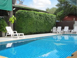 una piscina con sillas blancas y un seto en Forest Bungalows & Mama's Restaurant, en Chalong 