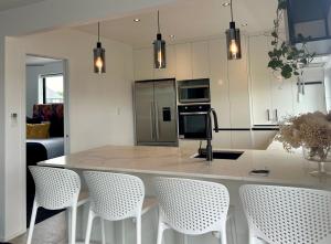 a kitchen with a large island with white chairs at Orewa Beachcomber in Orewa