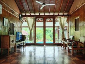 a living room with a ceiling fan and large windows at Javanese Joglo House by Malathi Ubud in Ubud