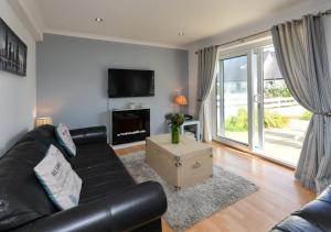 a living room with a black leather couch and a tv at 243 Cae Du in Abersoch