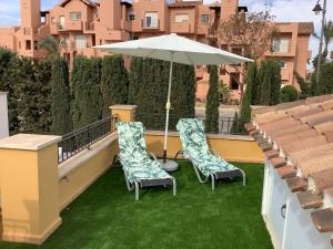 dwa krzesła i parasol na balkonie z trawą w obiekcie Mar menor golf detached Villa w mieście Torre-Pacheco