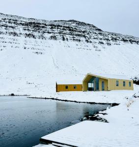 een geel gebouw aan de zijkant van een besneeuwde heuvel bij Fisk Club Cottages in Suðureyri