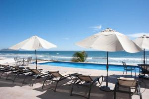 una piscina con sillas y sombrillas junto al océano en Spacious Apartment with Private Balcony & Ocean View - Brujas en Mazatlán