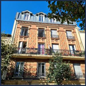 a tall brick building with windows and a balcony at Perle Haussmannienne 1900 - Cosy - Centre ville in La Garenne-Colombes