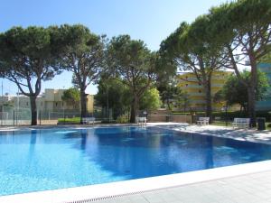 uma piscina com árvores e um edifício ao fundo em Relax and chill by the pool - Beahost em Bibione