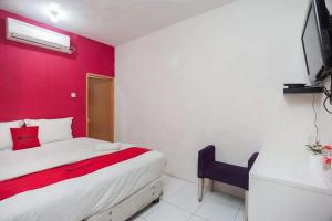 - une chambre dotée d'un mur rouge avec un lit et une chaise dans l'établissement Mega Stay near Mall Kelapa Gading, à Jakarta