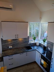 a kitchen with white cabinets and a sink and two windows at Leśny Zakątek-Domek Dąb in Parchowo