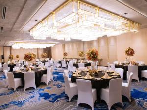 a banquet hall with tables and white chairs and a large chandelier at Admiral Hotel Manila - MGallery in Manila