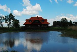 a house with a red roof next to a lake at Dwór Łabędzie w Kiermusach in Kiermusy