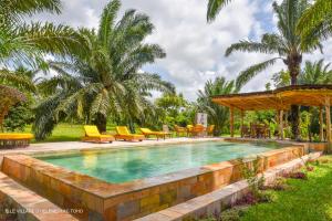 a swimming pool in a resort with yellow chairs and palm trees at LE VILLAGE D'HÉLÈNE - Natura Resort in Ouidah