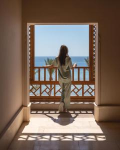The Makadi Spa Hotel - Couples Only 18 Years Plus في الغردقة: امرأة تقف على شرفة تطل على المحيط