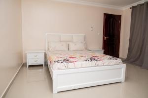 a white bedroom with a bed and a nightstand at Casa Chico Rosa in Luanda