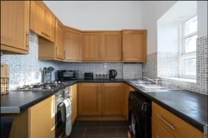 cocina con armarios de madera y encimera negra en 2 Bed Flat Prenton - Apartment 3 en Birkenhead