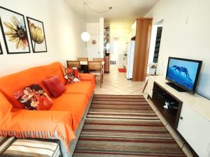 uma sala de estar com um sofá laranja e uma televisão de ecrã plano em Apto com sacada e churrasq 100m Praia Brava COI302 em Florianópolis
