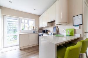 una cocina con armarios blancos y sillas verdes en Garden Flat short walk to Kingston & Richmond Park, en Strawberry Hill