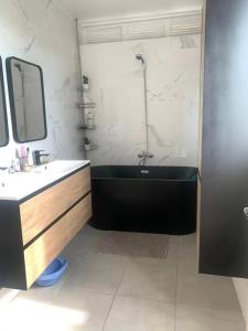 La salle de bains est pourvue d'une baignoire noire et d'un lavabo. dans l'établissement Appartement spacieux, à Sainte-Clotilde
